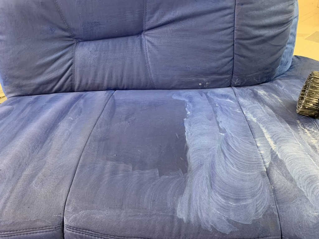 Reinigung eines blauen Stoffsofas mit Bürste und Schaum